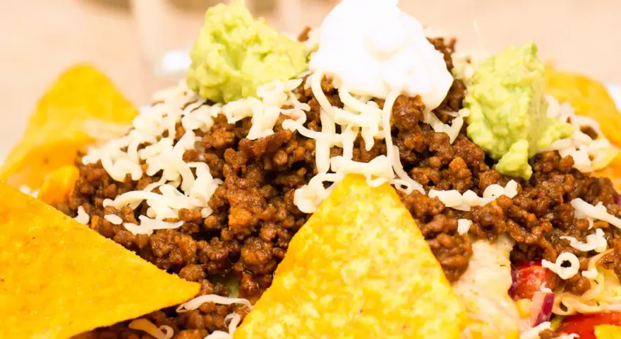 Schichtsalat mit Hackfleisch, Käse, Guacamole und saurer Sahne, garniert mit knusprigen Nachos.