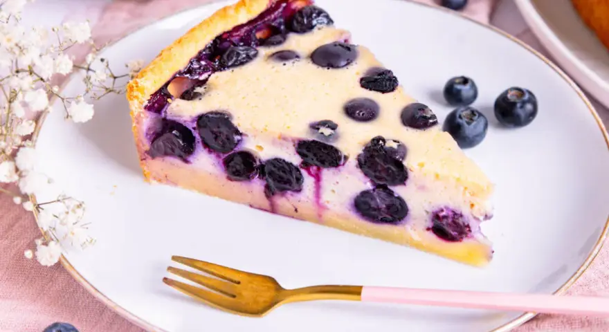 Ein Stück Blaubeerkuchen auf einem Teller, inspiriert von Landfrauen Kuchen Rezepten. Mit frischen Blaubeeren und zarter Füllung.