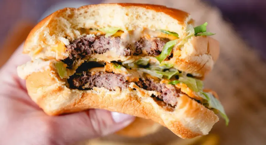 Ein saftiger Burger mit zwei Rindfleisch-Patties, Salat und der unverwechselbaren Big Mac Sauce, gehalten in einer Hand.