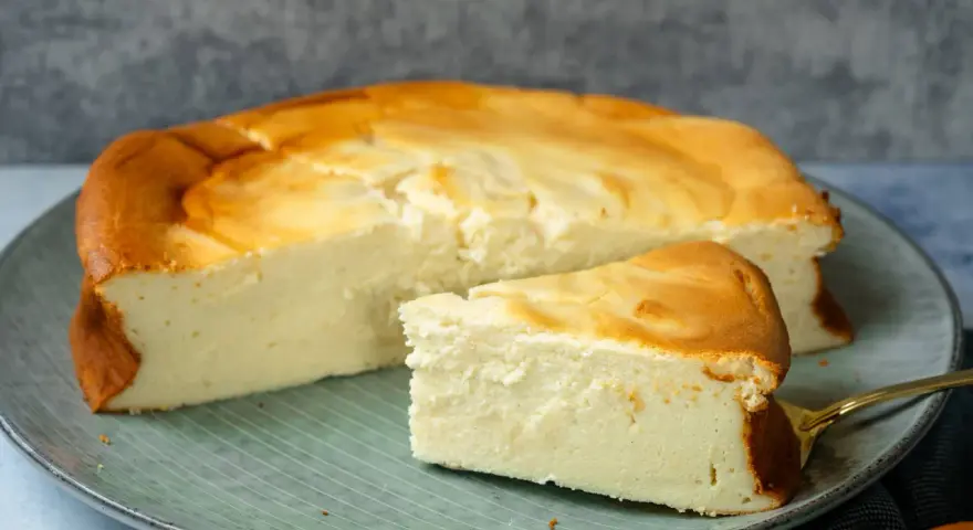 Saftiger Kuchen mit 250g Quark und Vanillepudding, goldbraun gebacken, auf einem Teller mit einem Stück daneben.