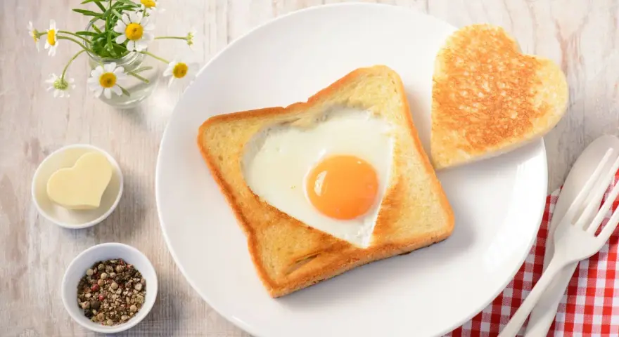 Herzförmiger Toast mit Ei, daneben ein Herzbutterstück und ein Herz-Toast. Ein liebevolles Frühstück.