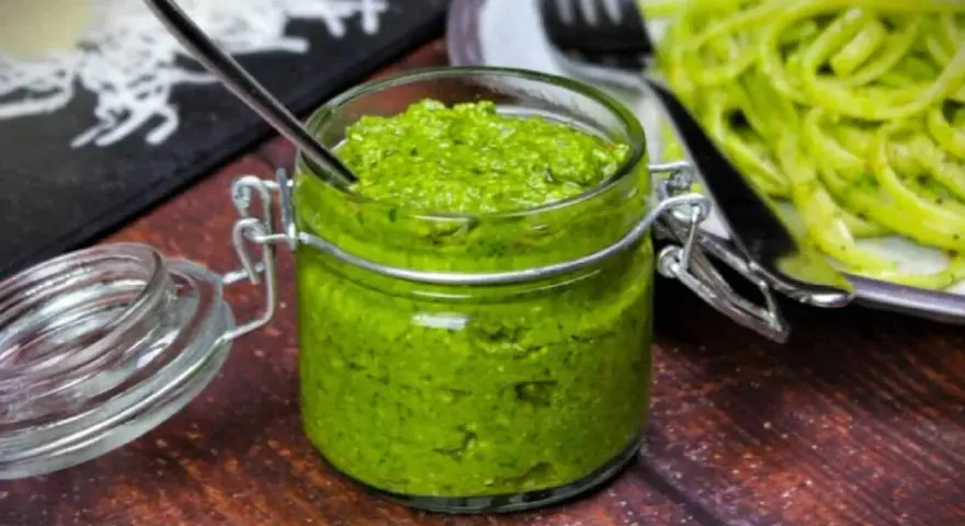 Frisches Rucola Pesto in einem Glas mit Löffel, daneben Pasta.