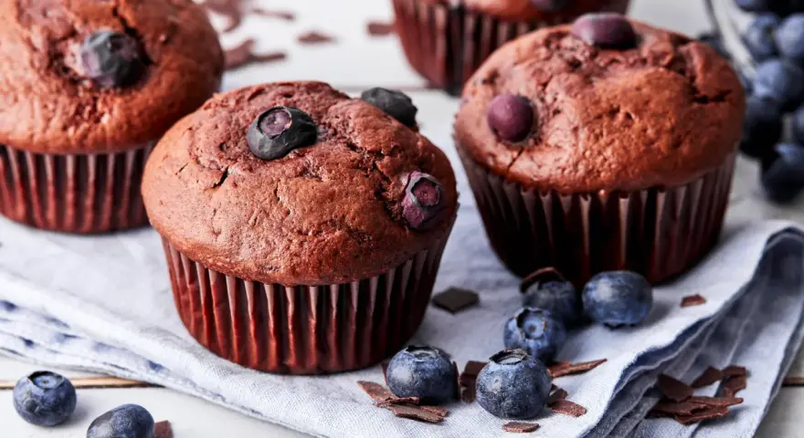 Saftige schoko blaubeer muffins, garniert mit frischen Blaubeeren und Schokostückchen, liegen auf einem Leinentuch.