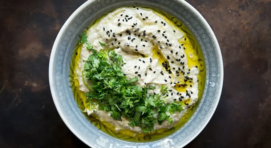 Cremiges Baba Ganoush, beträufelt mit Olivenöl, garniert mit frischer Petersilie und schwarzen Sesamkörnern.