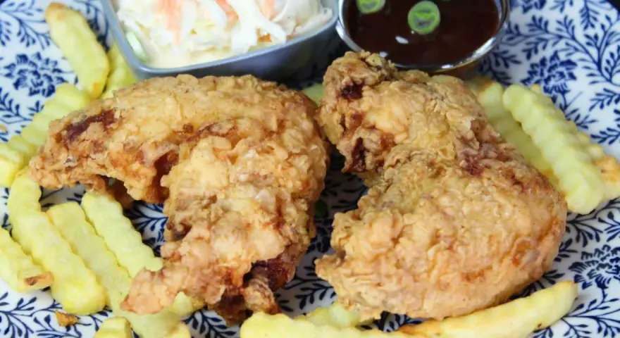 Knusprige chicken wings mit Pommes, Cole Slaw und BBQ-Sauce auf einem blau-weißen Teller.