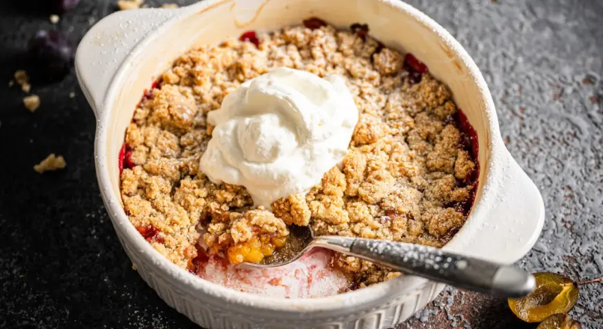 Ein köstlicher Zwetschgen Crumble mit Haferflocken, gekrönt mit einem Klecks Sahne, wartet darauf, genossen zu werden.