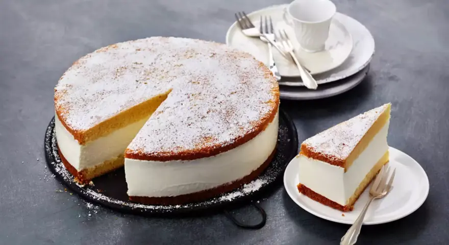 Eine köstliche Quark Sahne Torte, bestäubt mit Puderzucker, wartet darauf, genossen zu werden. Ein Stück ist bereits auf einem Teller angerichtet.