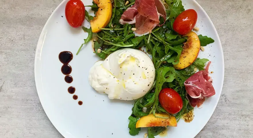 Salat mit Nektarinen, Burrata, Prosciutto und Kirschtomaten, garniert mit Balsamico-Dressing.