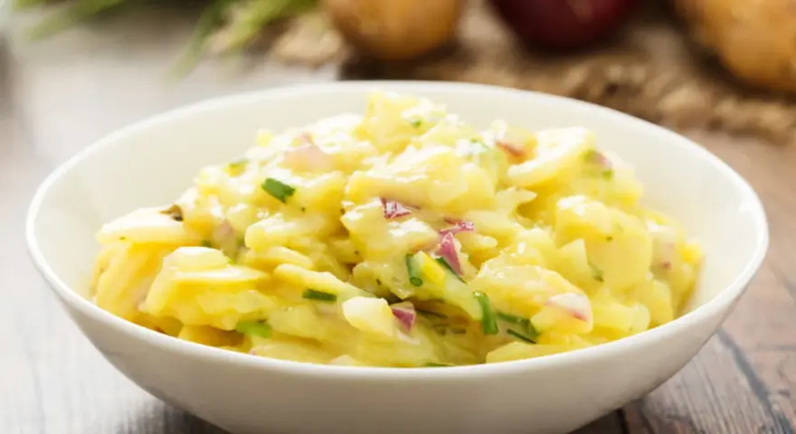 Omas Kartoffelsalat Rezept Original: Ein cremiger Kartoffelsalat mit Zwiebeln und Schnittlauch in einer weißen Schüssel, bereit zum Genießen.