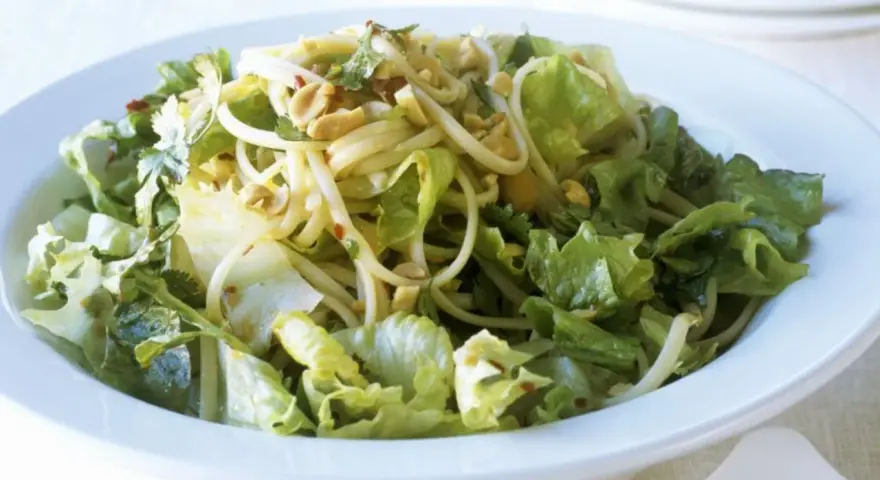 Ein leckerer Yum Yum Salat mit knackigem Eisbergsalat, Nudeln und Erdnüssen in einer weißen Schüssel.
