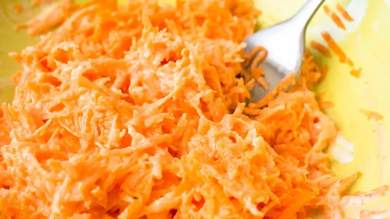 Fein geriebener Karottensalat mit cremigem Dressing. Eine Gabel liegt im Salat.