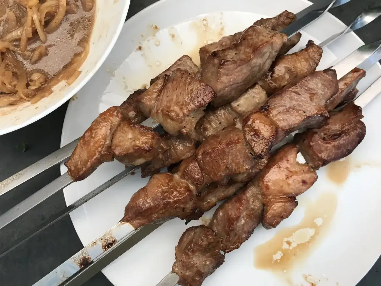 Saftige Fleischspie&szlig;e, die nach dem besten russischen Schaschlik Rezept zubereitet wurden. Dazu gibt es eine Sch&uuml;ssel mit marinierten Zwiebeln.