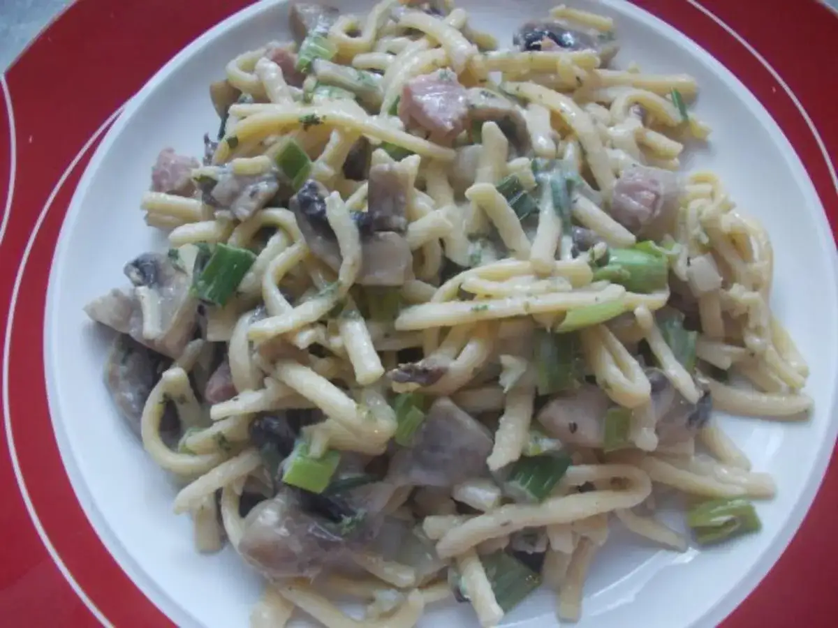 Nudeln mit Champignon Rahm Sauce, Pilzen, Speck und Lauchzwiebeln auf einem Teller.
