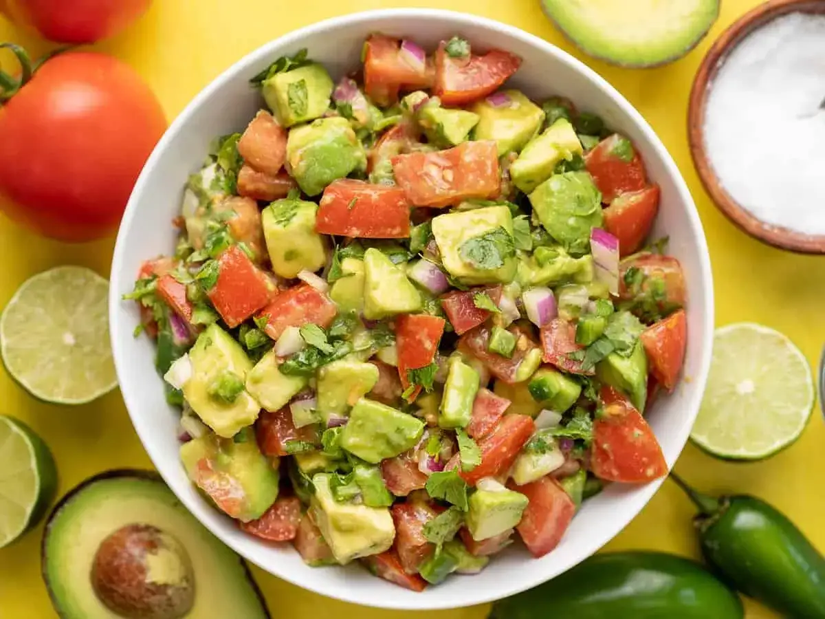 Frischer Avocado Tomaten Salat, garniert mit Koriander und Zwiebeln, daneben Limetten und Jalape&ntilde;os.