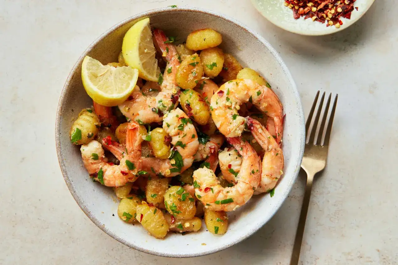 Sch&uuml;ssel mit Gnocchi mit Garnelen, garniert mit Petersilie und Zitronenspalten. Ein goldener Gabel liegt daneben.