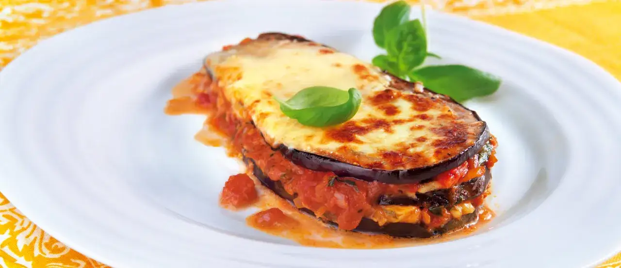Ein köstliches Melanzane Rezept original: geschichtete Aubergine mit Tomaten und geschmolzenem Käse, garniert mit Basilikum.