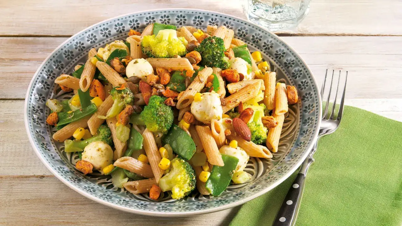 Bunter nudelsalat mit brokkoli, Mais, Erbsen und Mozzarella-Kugeln, garniert mit Mandeln und ger&ouml;steten Kernen.