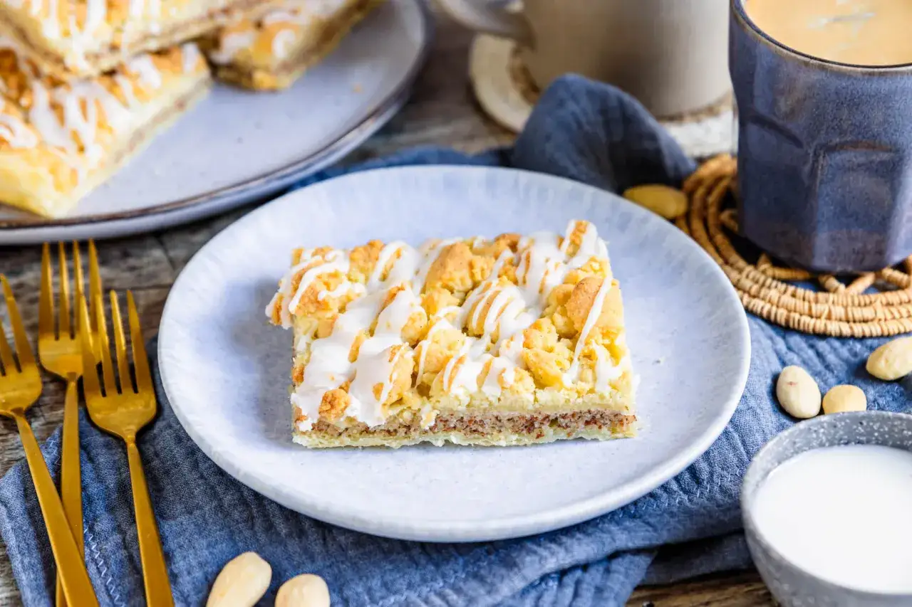 Ein St&uuml;ck Prasselkuchen, wie aus einem DDR-Rezept, mit Streuseln und Zuckerguss, serviert auf einem Teller mit Kaffee.
