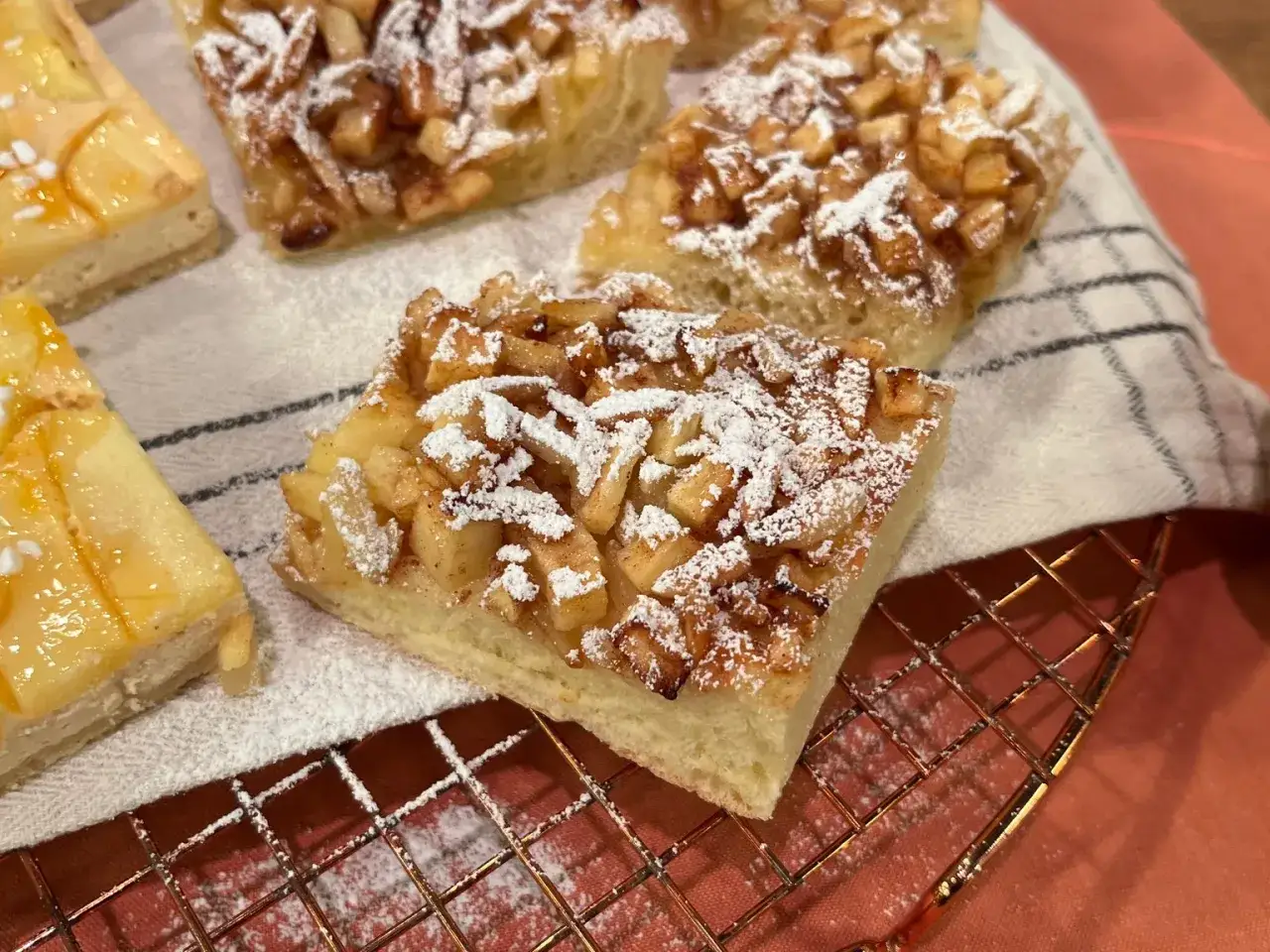Saftige Apfelkuchenst&uuml;cke, best&auml;ubt mit Puderzucker, wie bei den besten Landfrauen Kuchen Rezepten. Daneben ein St&uuml;ck mit Aprikosenmarmelade.