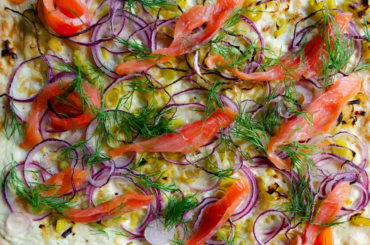 Flammkuchen mit Lachs und Cr&egrave;me fra&icirc;che, garniert mit roten Zwiebeln und Dill.