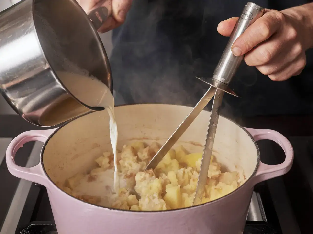Fl&uuml;ssigkeit wird in einen Topf mit Kartoffeln und Sellerie gegossen, um einen Kartoffel-Sellerie-Stampf zuzubereiten.