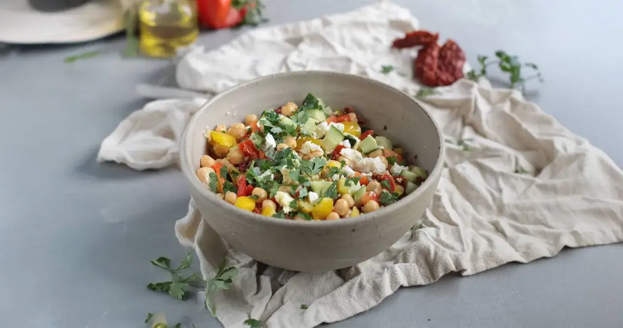 Frischer Kichererbsen Salat mit Gurke, Tomaten, Paprika und Feta, garniert mit Petersilie. Ein leichter und gesunder Genuss.