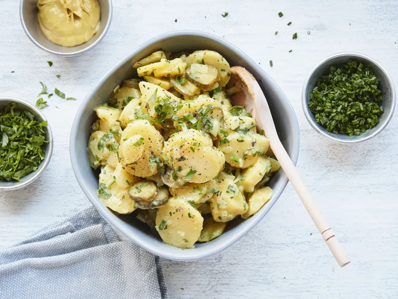 Ein k&ouml;stlicher Kartoffelsalat ohne Mayo, garniert mit frischer Petersilie und Schnittlauch. Daneben Sch&auml;lchen mit Senf und Kr&auml;utern.