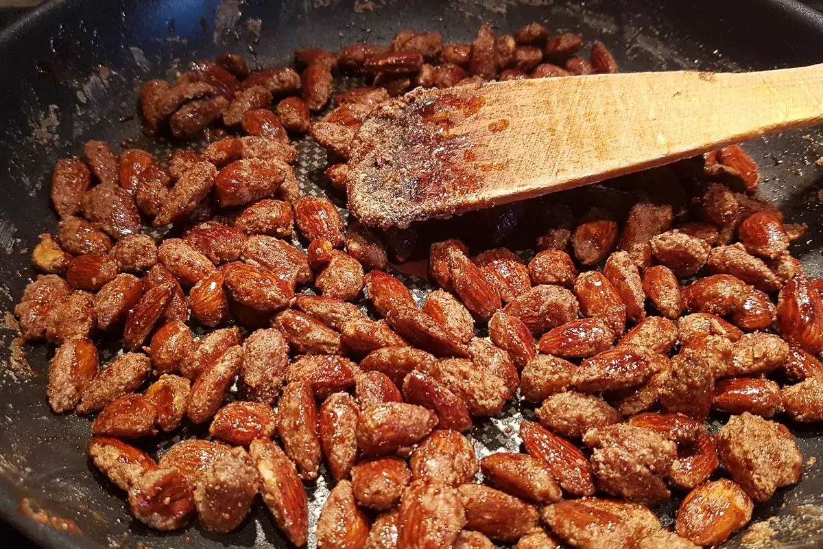 Gebrannte Mandeln in einer Pfanne, mit einem Holzspatel werden sie gewendet. Sie gl&auml;nzen s&uuml;&szlig; und verlockend.