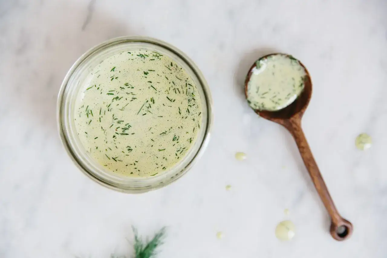 Cremiges Salatdressing ohne Essig, mit frischem Dill verfeinert, in einem Glas und auf einem Holzl&ouml;ffel.