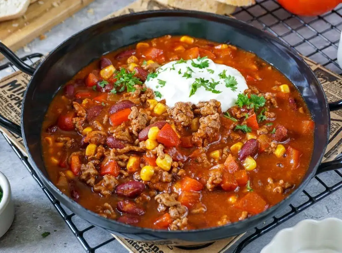 Herzhaftes Chili con Carne mit Hackfleisch, Kidneybohnen, Mais und Paprika, garniert mit einem Klecks Sauerrahm und Petersilie.