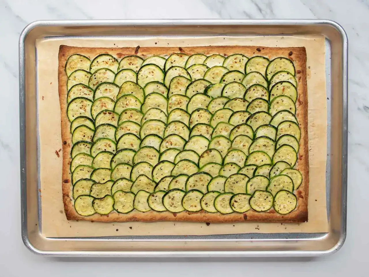 Rechteckige Zucchini Scarpaccia auf einem Backblech, mit d&uuml;nnen Zucchinischeiben belegt und mit Pfeffer bestreut.