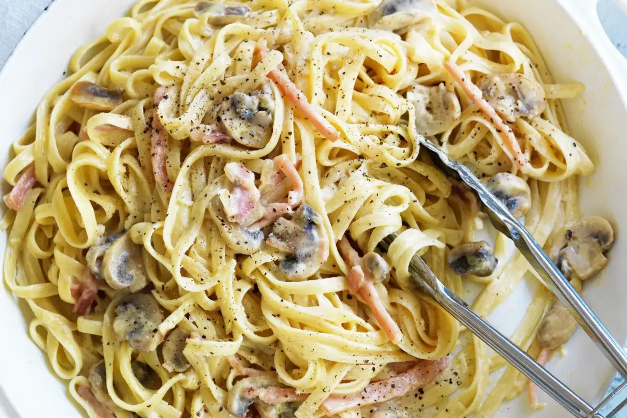 Cremige Pasta mit Pilzen und Speck, eine k&ouml;stliche Carbonara ohne Ei, bestreut mit schwarzem Pfeffer.