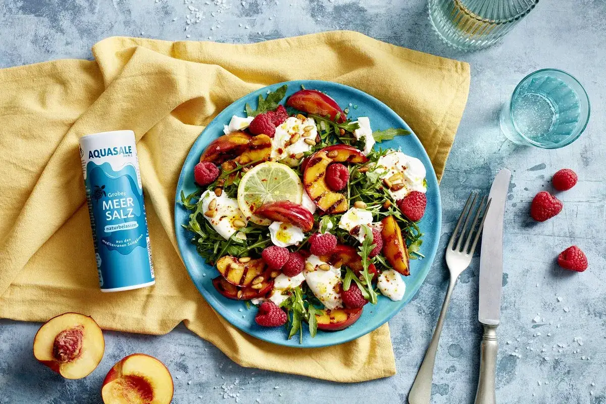 Salat mit Nektarinen, Rucola, Mozzarella und Himbeeren, garniert mit Pinienkernen und Zitronenscheibe. Perfekt mit grobem Meersalz.