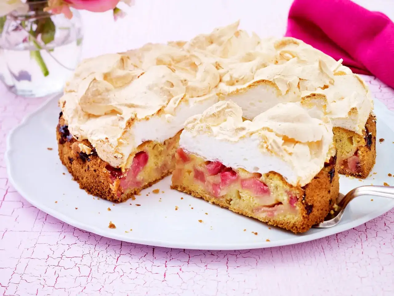 Ein saftiger Rhabarberkuchen mit einer luftigen Baiserhaube, auf einem wei&szlig;en Teller, bereit zum Genie&szlig;en.