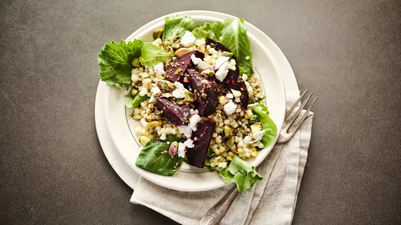 Ein bunter rote beete couscous salat mit Feta und Pistazien, garniert mit frischem Grün.