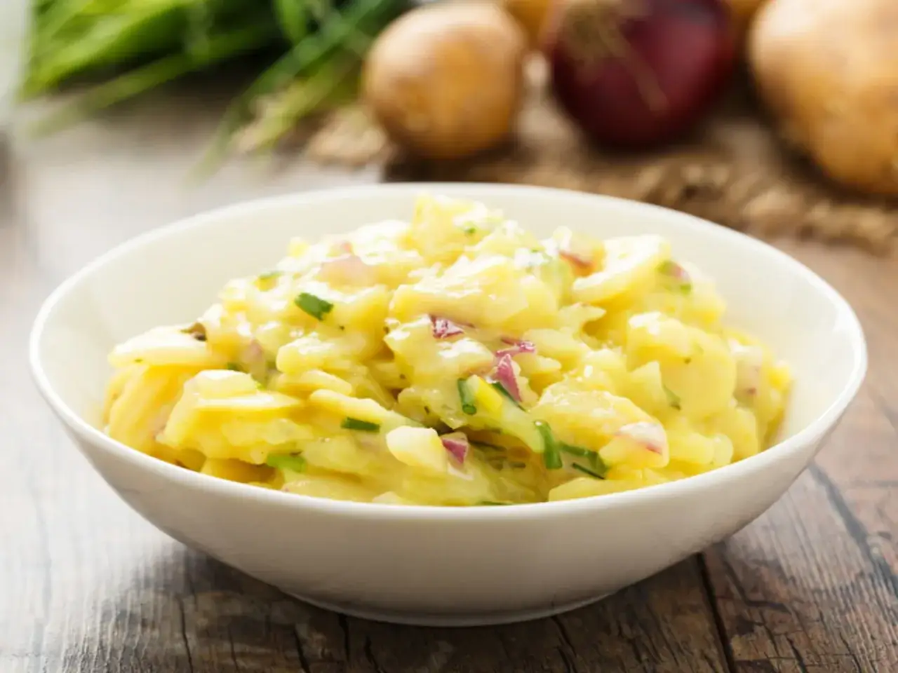 Omas Kartoffelsalat Rezept Original: Ein cremiger Kartoffelsalat mit Zwiebeln und Schnittlauch in einer weißen Schüssel.