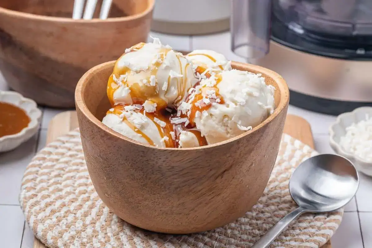 Kokoseis selber machen mit Eismaschine: Cremiges Eis mit Kokosraspeln und Karamell-So&szlig;e in einer Holzschale.
