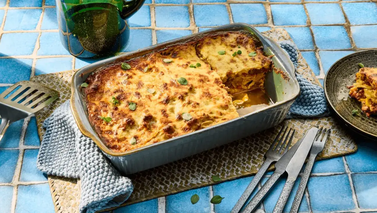Herzhaftes Moussaka mit Zucchini, goldbraun gebacken, dampft in einer Auflaufform. Ein St&uuml;ck auf einem Teller daneben l&auml;dt zum Genuss ein.