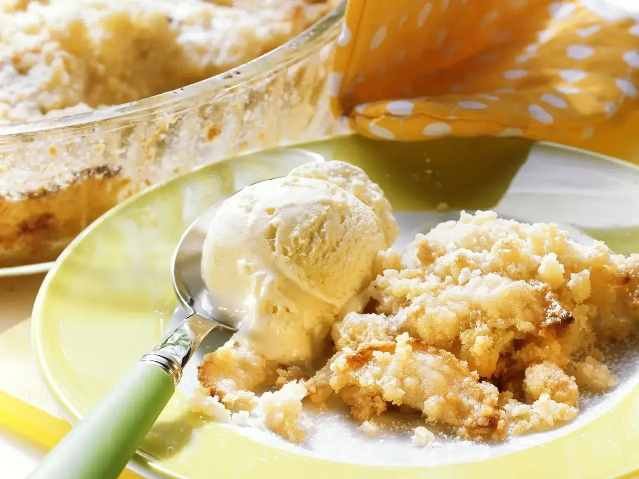Ein warmer Apfel Crumble mit einer Kugel Vanilleeis auf einem gelben Teller.