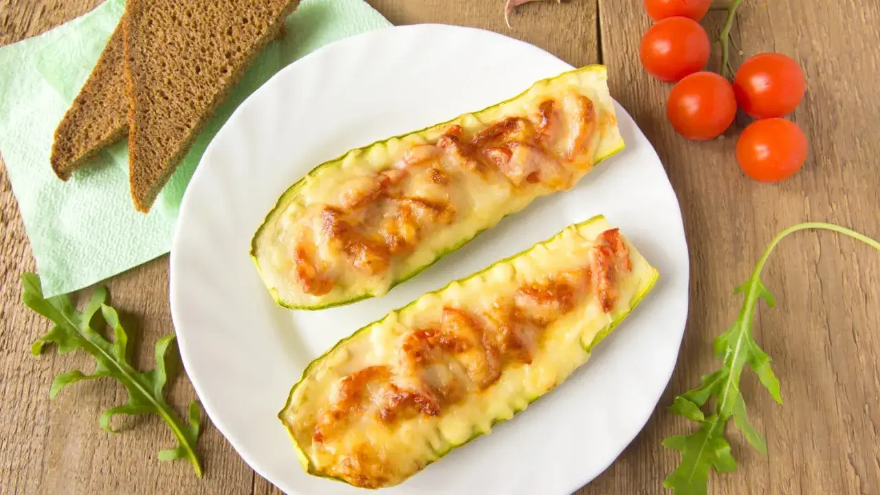 Zucchini mit Feta im Ofen, &uuml;berbacken und goldbraun, serviert mit Brot und Tomaten.