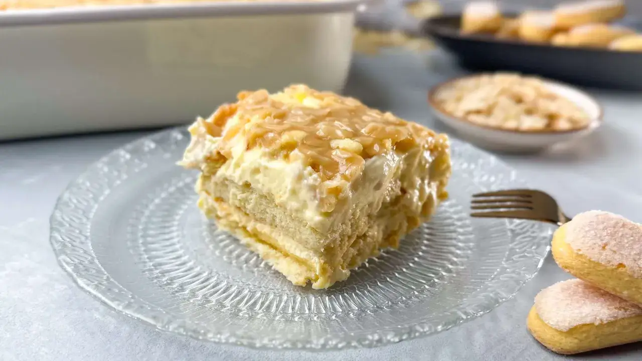 Ein St&uuml;ck Bienenstich Tiramisu auf einem Glas Teller, garniert mit karamellisierten Mandeln.
