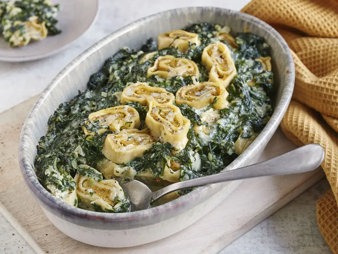 Herzhafter Maultaschen Auflauf mit Spinat und cremiger Sauce, garniert mit frisch gemahlenem Pfeffer.