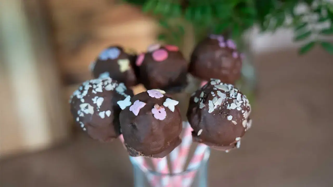 Leckere cake pops aus kuchenresten, verziert mit bunten Streuseln und Mandelsplittern, stecken in rosa-wei&szlig;en Papierstrohhalmen.