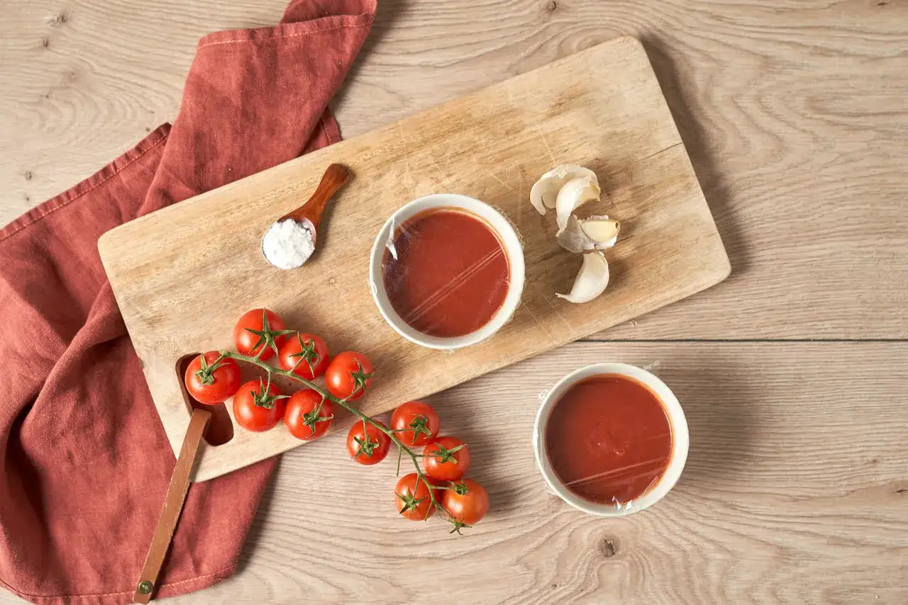 Zutaten f&uuml;r ketchup selber machen: frische Tomaten, Knoblauch, Salz und eine rote Serviette auf einem Holzbrett.