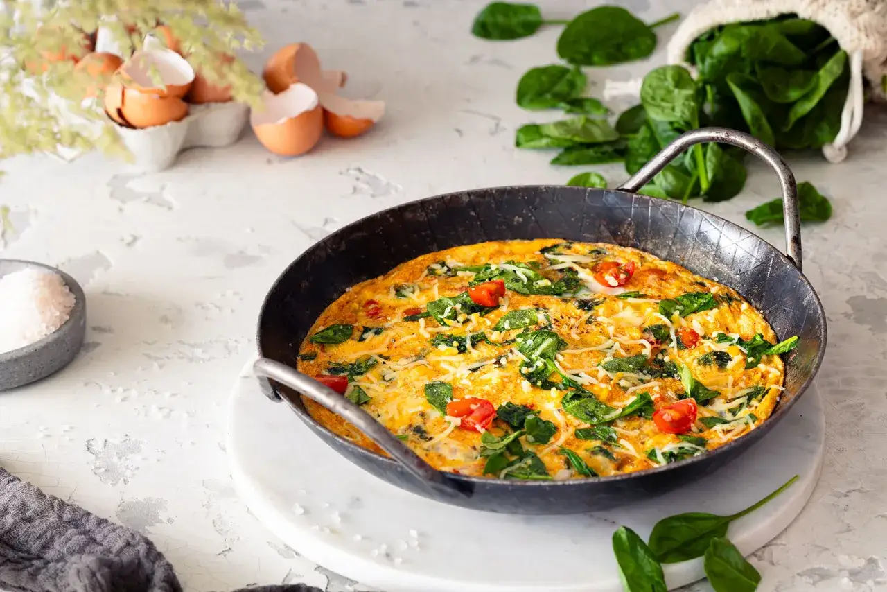 Herzhafte Hauptspeise: Frittata mit vielen Eiern, Spinat und Tomaten, bestreut mit K&auml;se.
