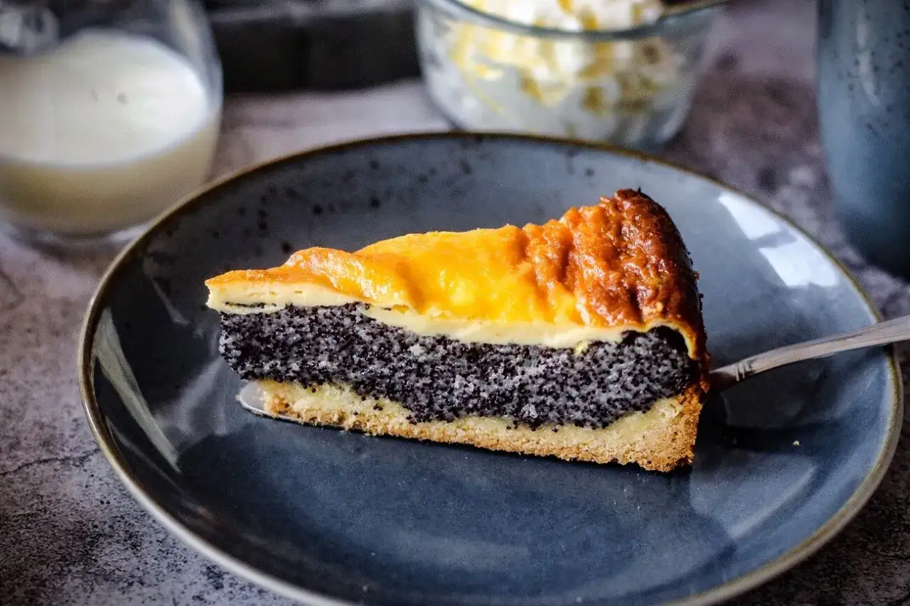 Ein St&uuml;ck saftiger Mohnkuchen mit Schmand und goldbrauner Kruste auf einem blauen Teller.