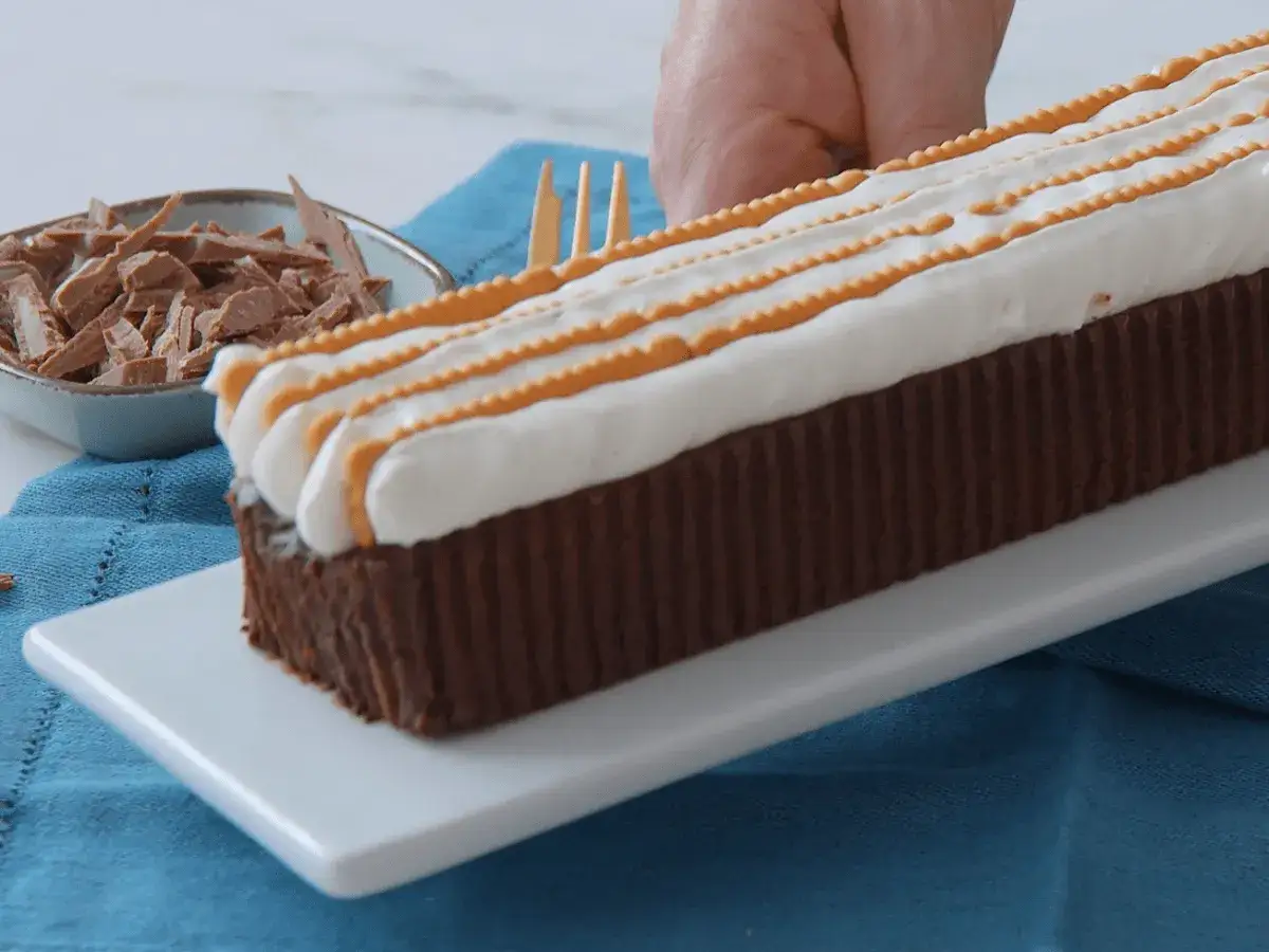 Ein leckerer Kalter Hund mit Schokolade und Sahne, verziert mit orangen Streifen. Daneben eine Schale Schokostreusel.