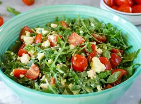 Frischer Rucolasalat mit saftigen Tomaten und cremigem Käse in einer türkisfarbenen Schüssel.