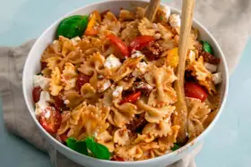 Ein köstlicher Nudelsalat mit Farfalle, frischen Tomaten, Mozzarella und sonnengetrockneten Tomaten, garniert mit Basilikum.