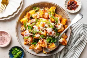 Kartoffelsalat mal anders: knusprige Kartoffelspalten mit cremiger Sauce, Frühlingszwiebeln und roten Zwiebelringen in einer rustikalen Schüssel.